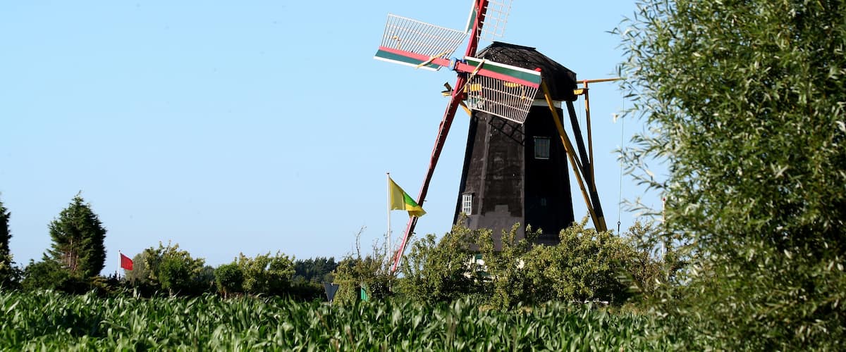 A windmill with a red and white structure, surrounded by greenery and a clear blue sky.