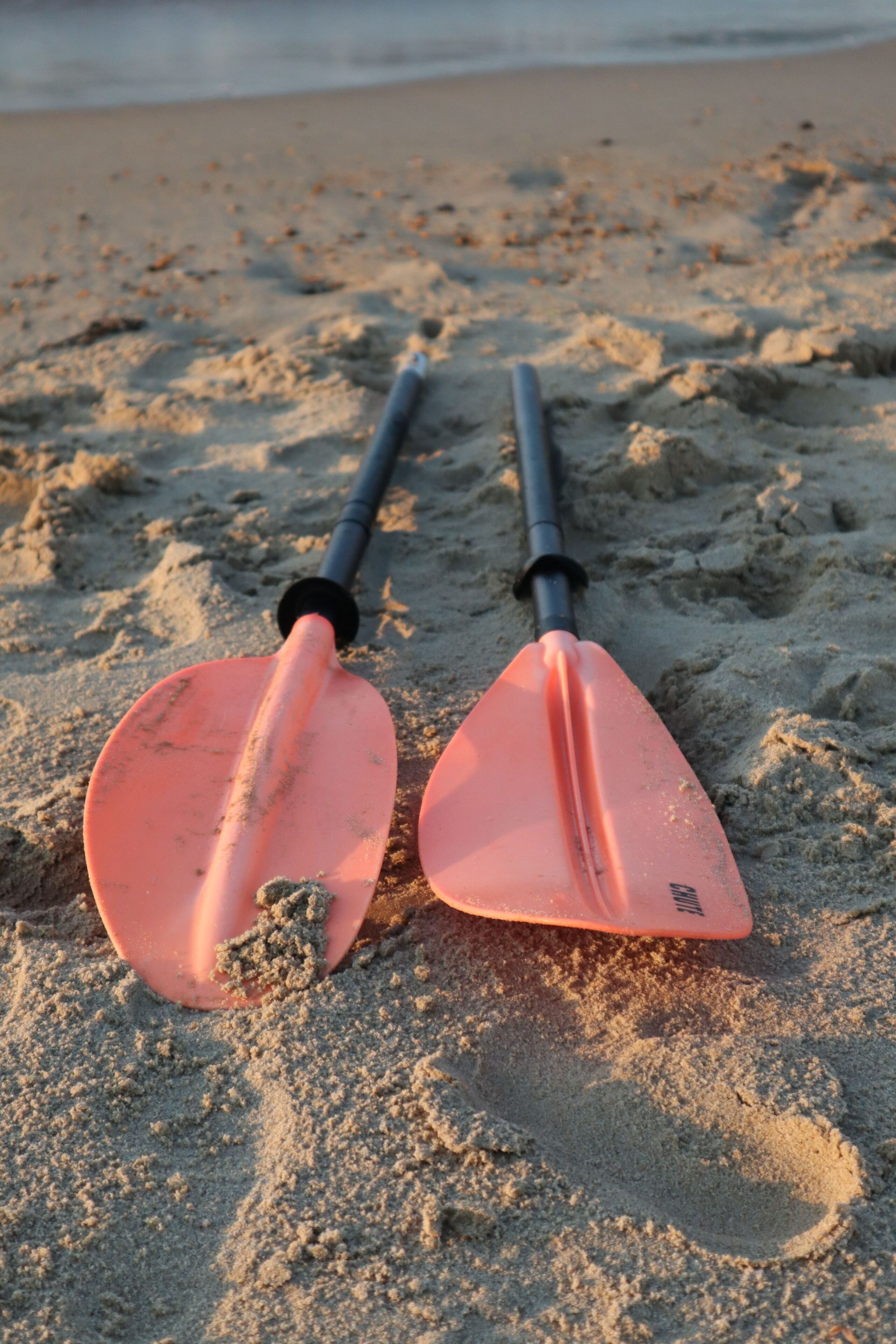 Two orange paddleboards on a sandy beach with a black pole between them.