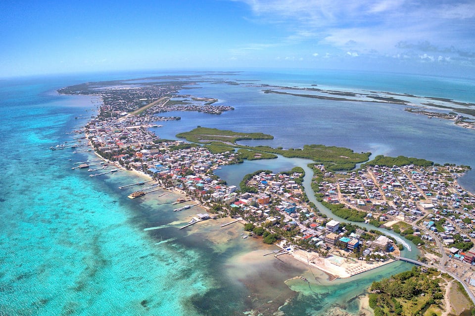 An aerial view of a coastal town with clear turquoise waters, a long beachfront, and a dense cluster of buildings.
