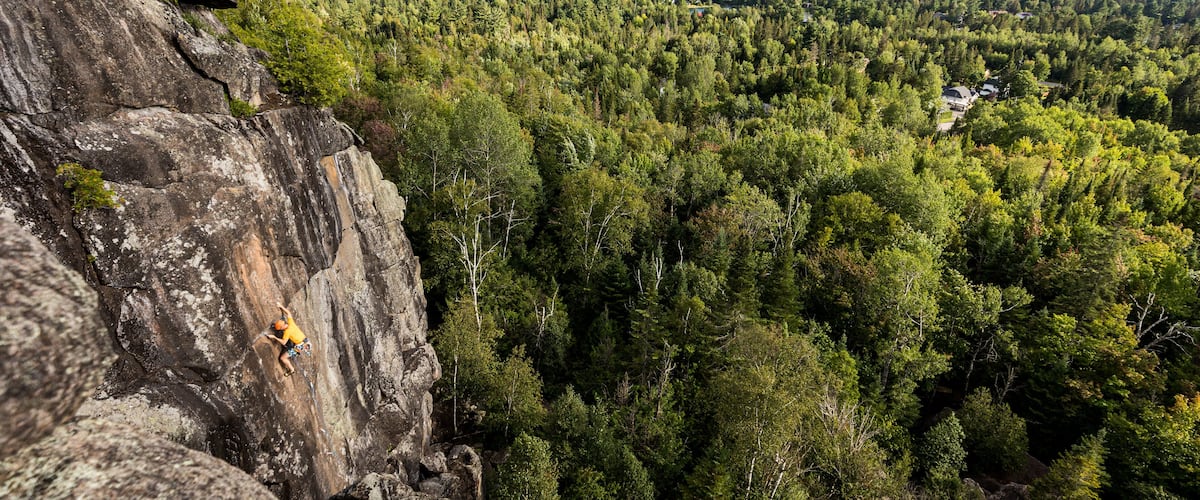 A climber on a rock face with a forested valley below.