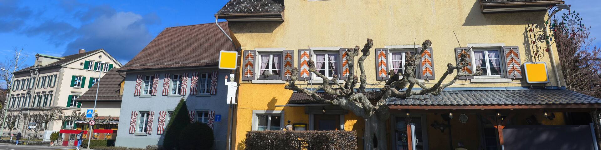 A yellow building with red and white striped shutters, a traditional European architectural style, and a clear blue sky in the background.