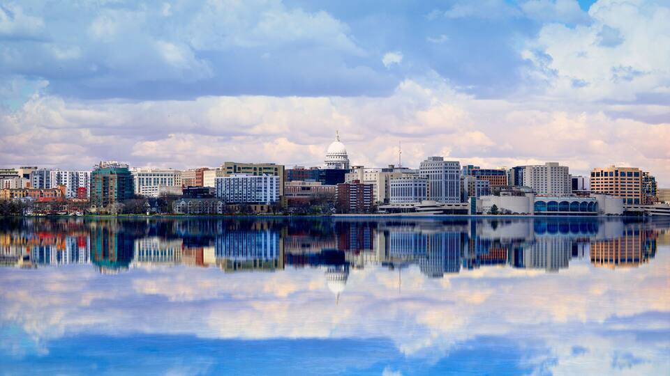 A city skyline with a prominent white dome building, reflecting in a calm body of water.