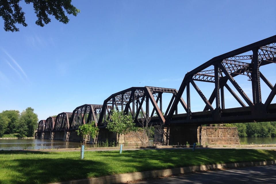 A series of large, rusted steel bridges over a river, surrounded by grassy areas and trees.