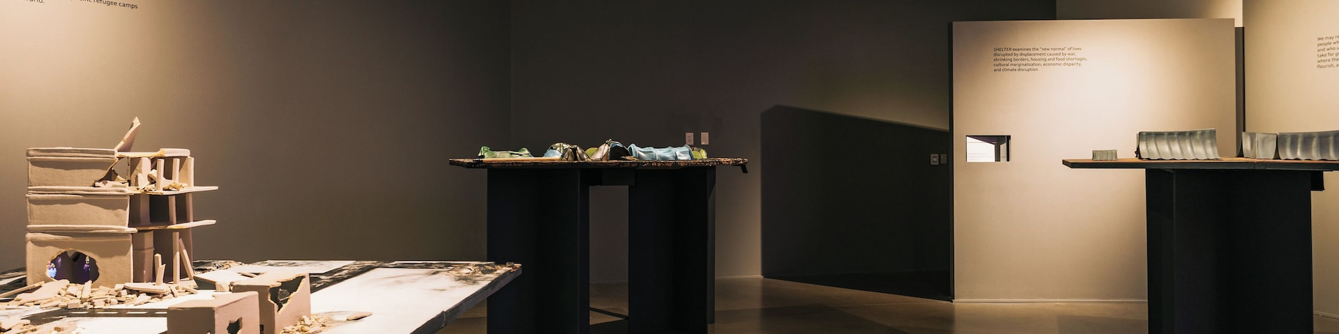 Exposição de arte com esculturas e instalações dispostas sobre mesas.