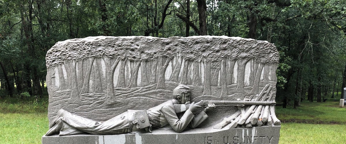 A stone monument with a soldier lying down, holding a rifle, and a log.