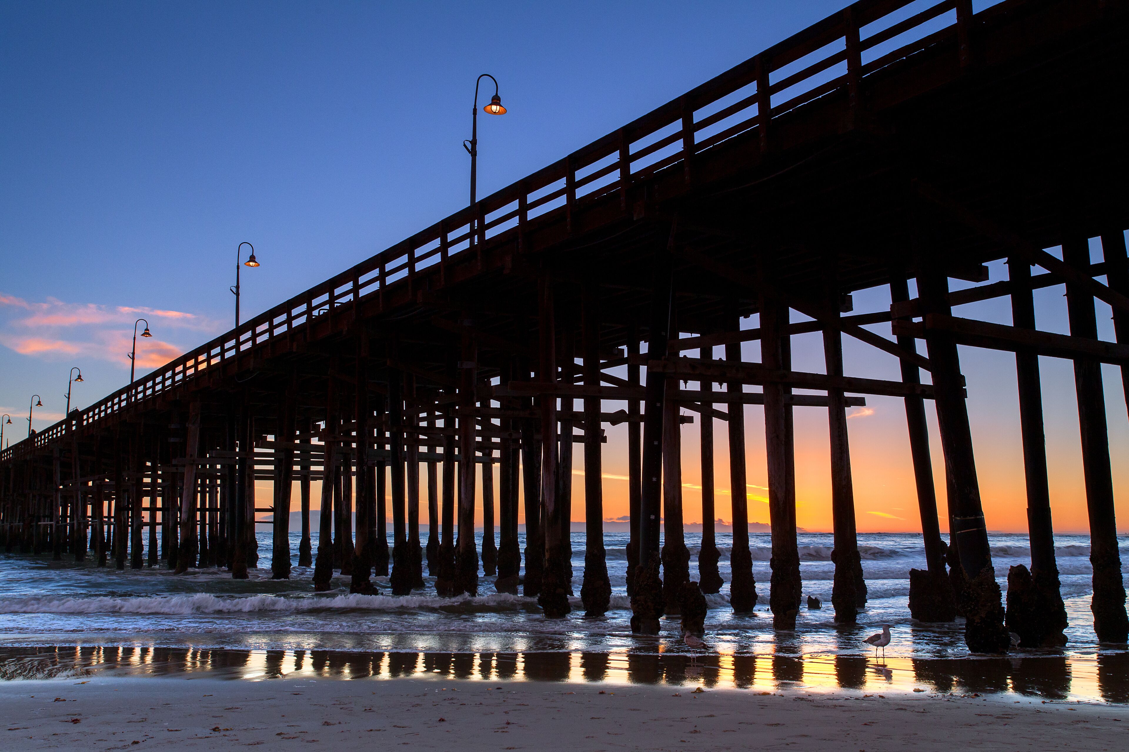 A pier extending into the ocean at sunset with a clear sky.