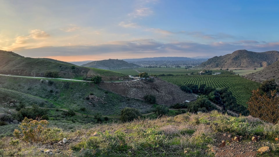 A valley with a road, green fields, and mountains in the background.