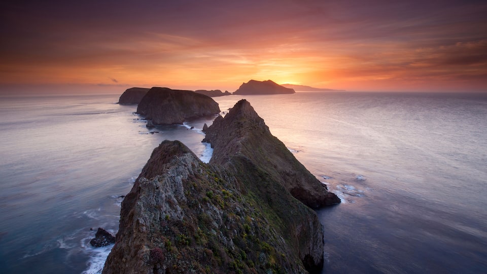 A coastal landscape with prominent rock formations and a sunset over the ocean.