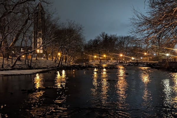 A river reflecting lights, surrounded by bare trees and a snow-covered path.