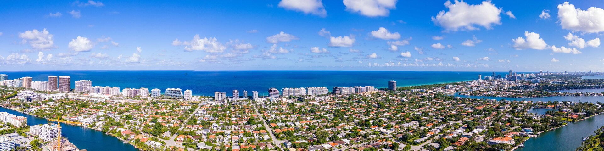 A coastal cityscape with dense residential areas, a marina, and a clear blue sky.