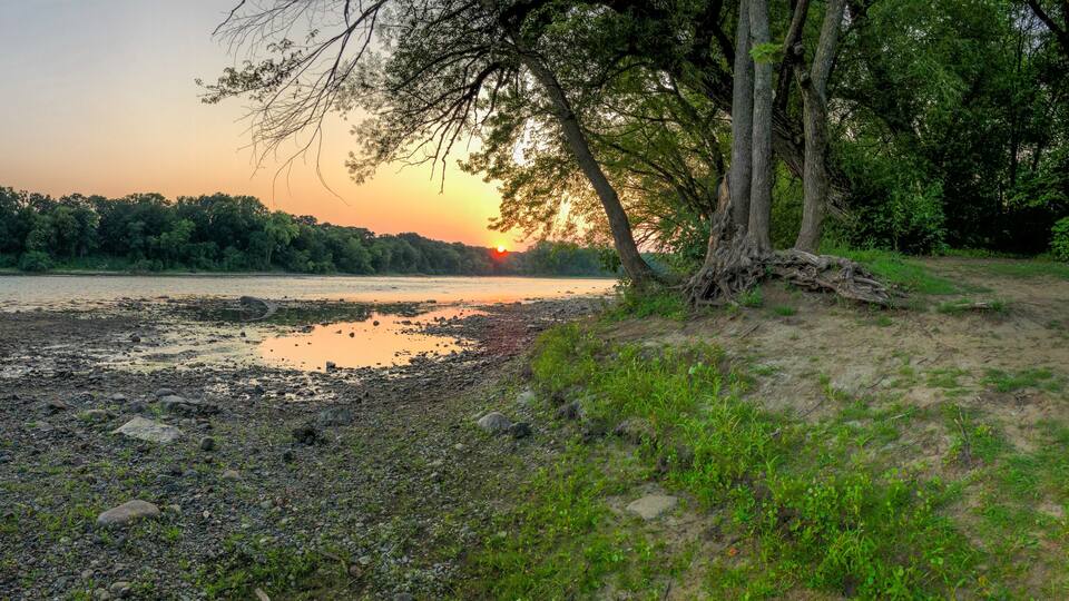 A sunset over a river with a rocky shoreline and trees.