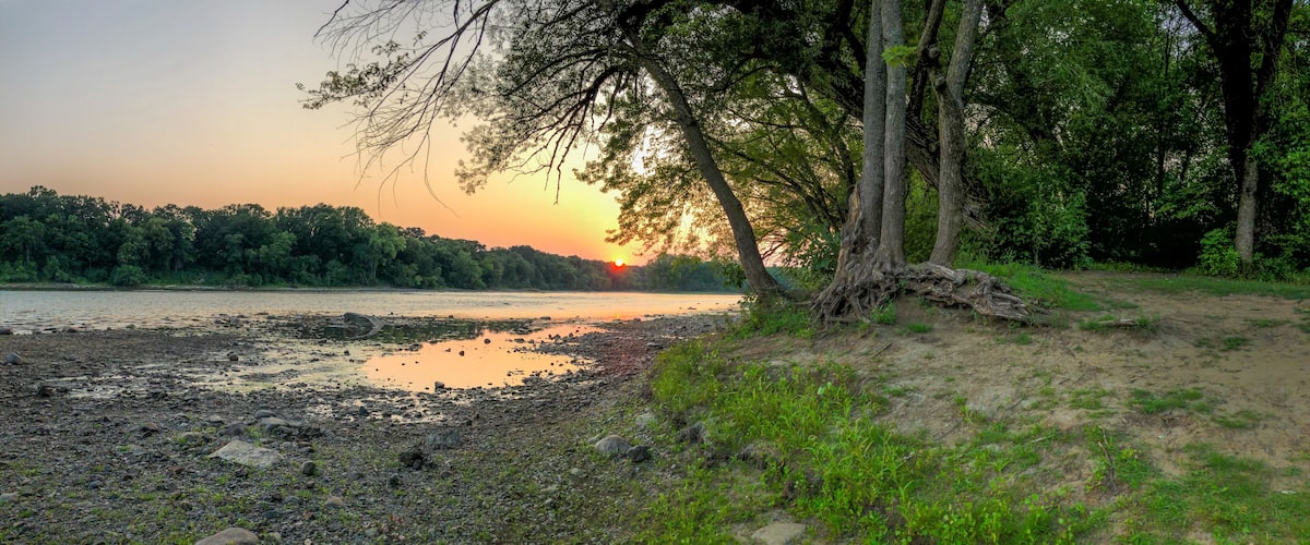 A sunset over a river with a rocky shoreline and trees.