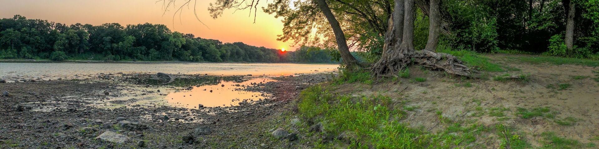 A sunset over a river with a rocky shoreline and trees.