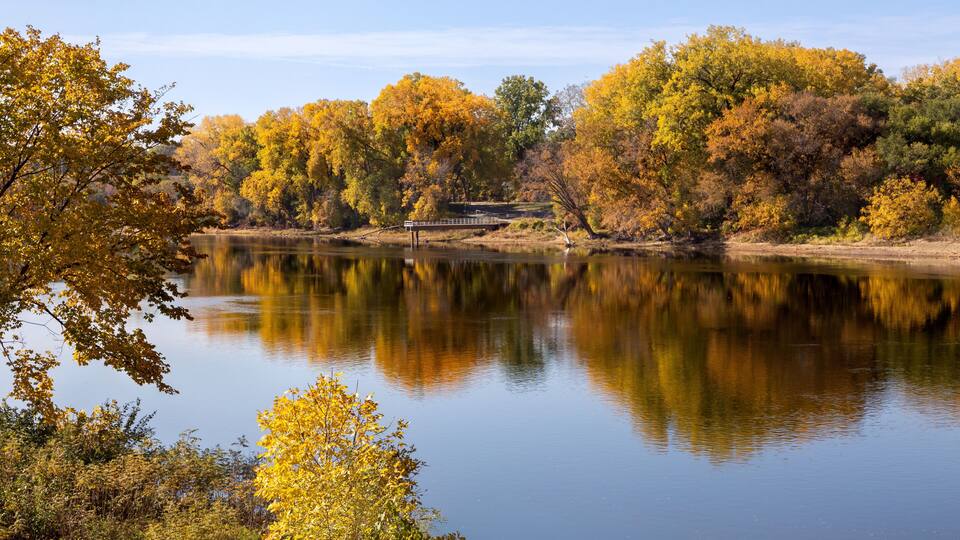 A calm lake surrounded by autumn-colored trees and a small bridge.