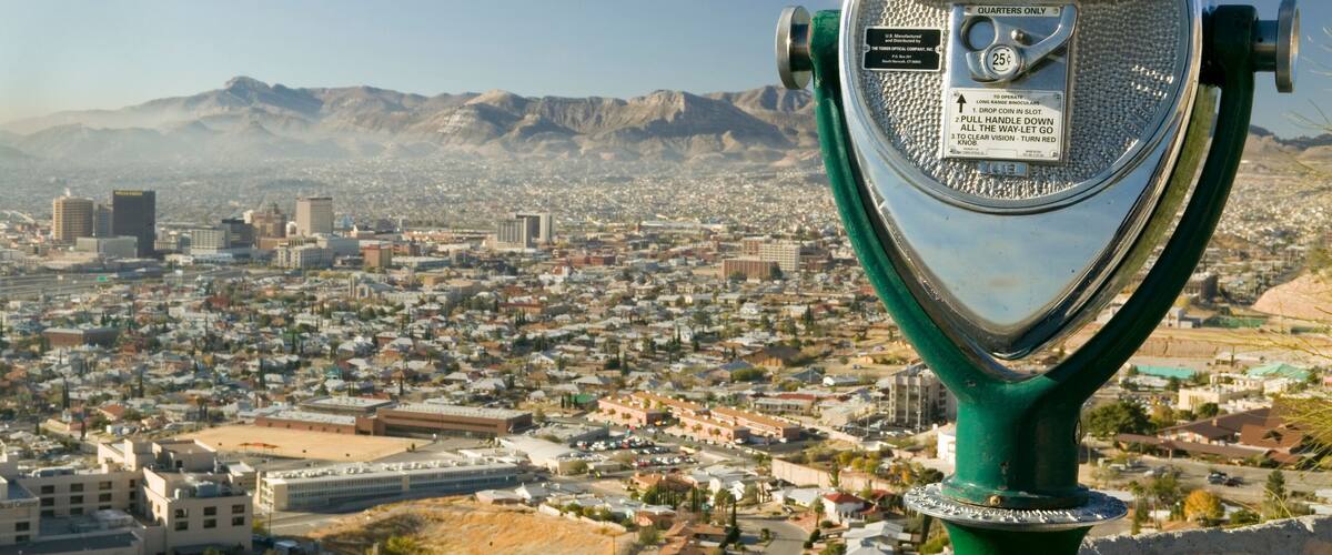 A telescope overlooking a cityscape with mountains in the background.