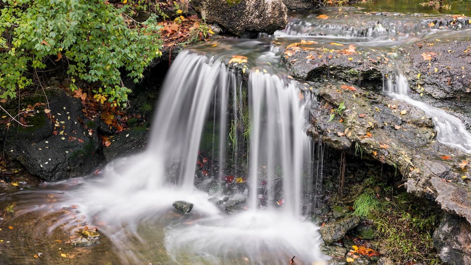 A waterfall cascading over rocks in a forested area with autumn leaves.
