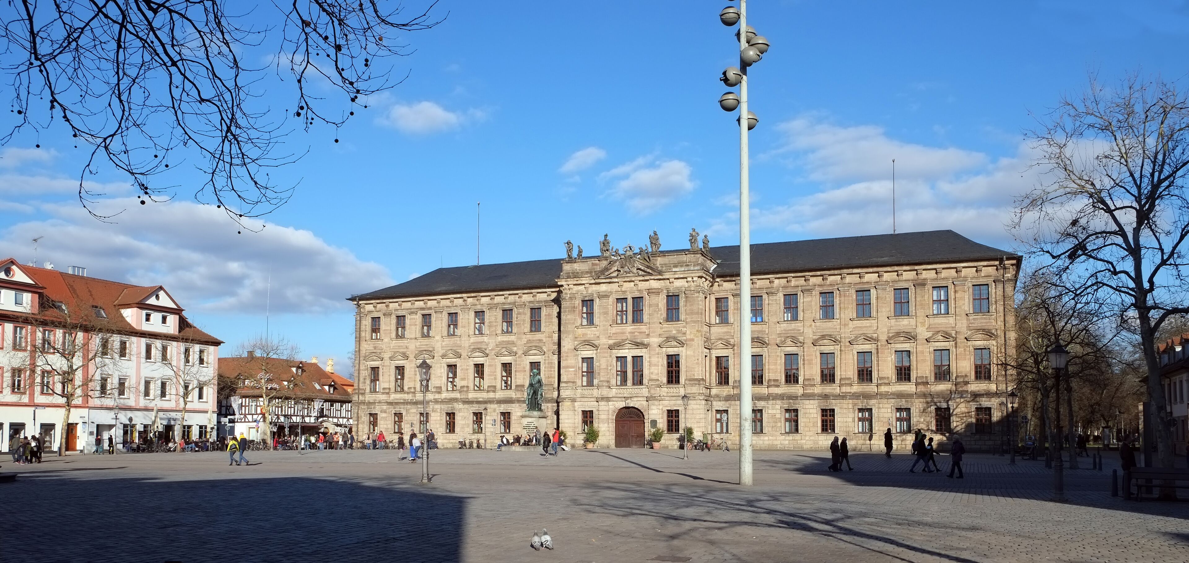 A historic building with classical architecture, a cobblestone square, and leafless trees.