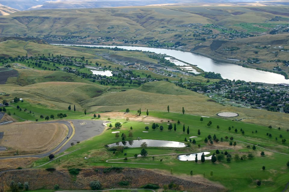 Un río serpentea entre colinas ondulantes, un campo de golf y un pequeño pueblo.