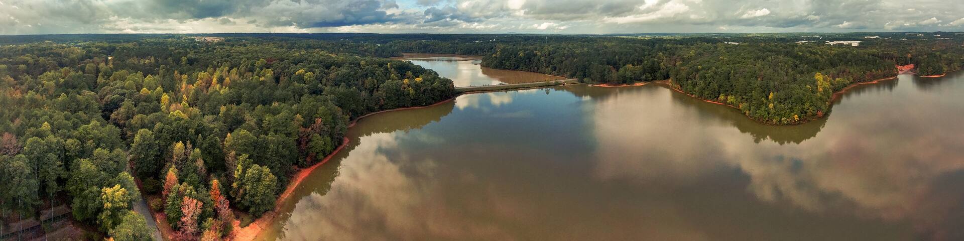 a breathtaking panoramic aerial shot of the still lake waters and vast miles of lush green and autumn colored trees with powerful cloud formations and blue sky at Sweetwater Creek State Park