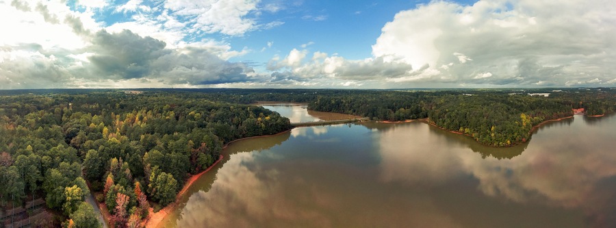 a breathtaking panoramic aerial shot of the still lake waters and vast miles of lush green and autumn colored trees with powerful cloud formations and blue sky at Sweetwater Creek State Park