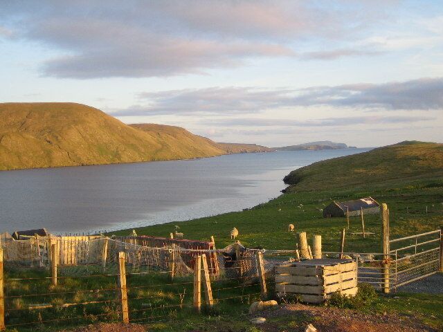 A coastal landscape with a fenced area, a small building, and a hill in the background.