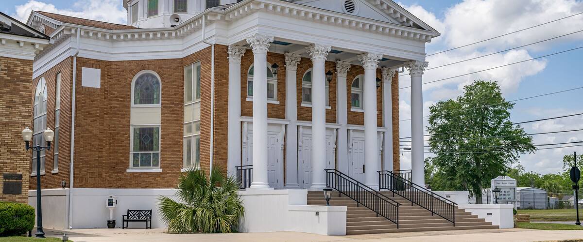A historic building with a golden dome, white columns, and a staircase leading to the entrance.