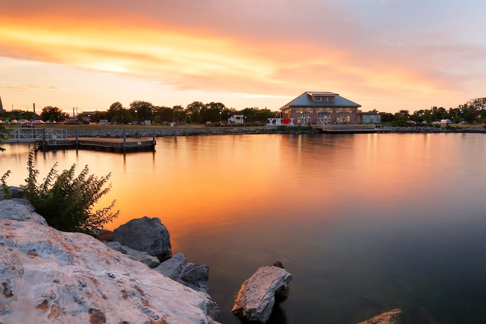 A calm lake at sunset with a building and dock in the background.