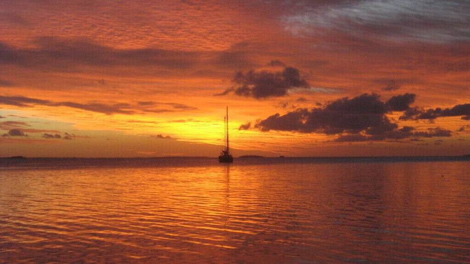 A sunset over a calm sea with a sailboat in the distance.
