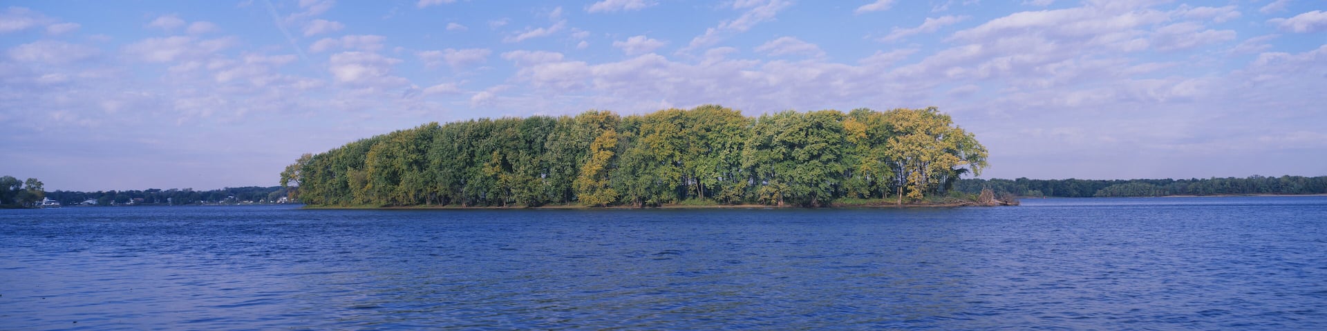 A small island surrounded by a calm lake with dense green foliage and a clear blue sky.