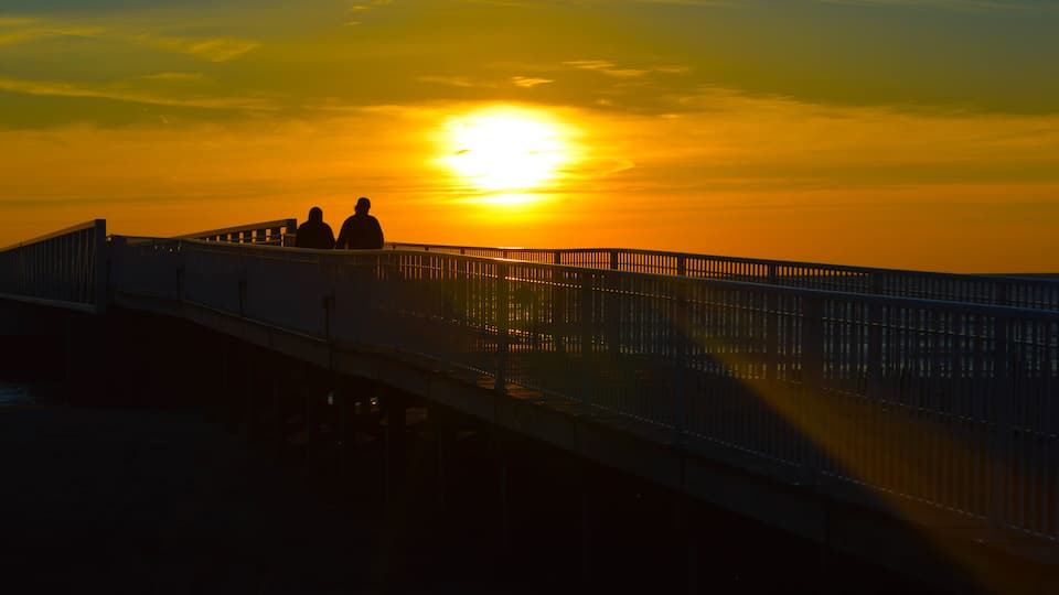 A sunset over a bridge with two silhouetted figures.