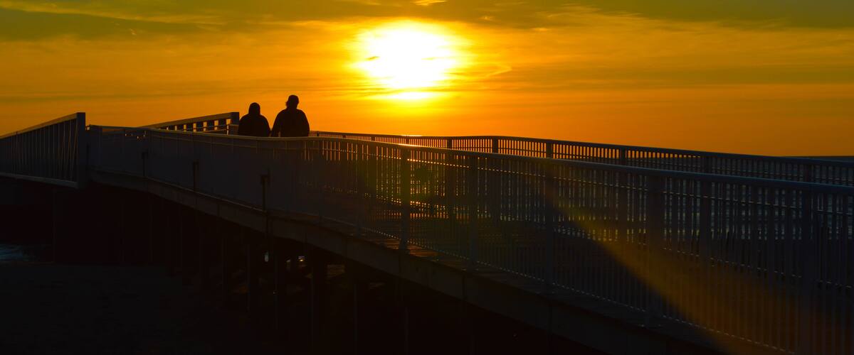 A sunset over a bridge with two silhouetted figures.