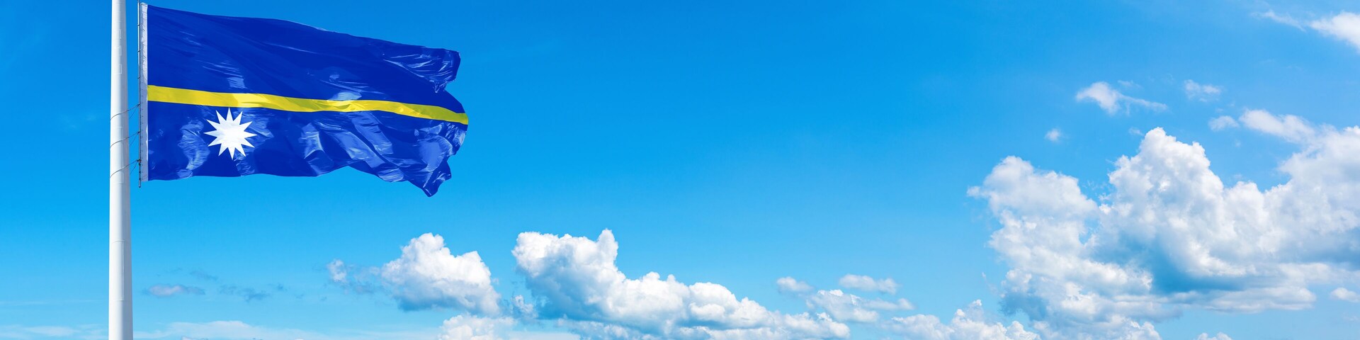 Nauru flag waving on a blue sky in beautiful clouds - Horizontal banner