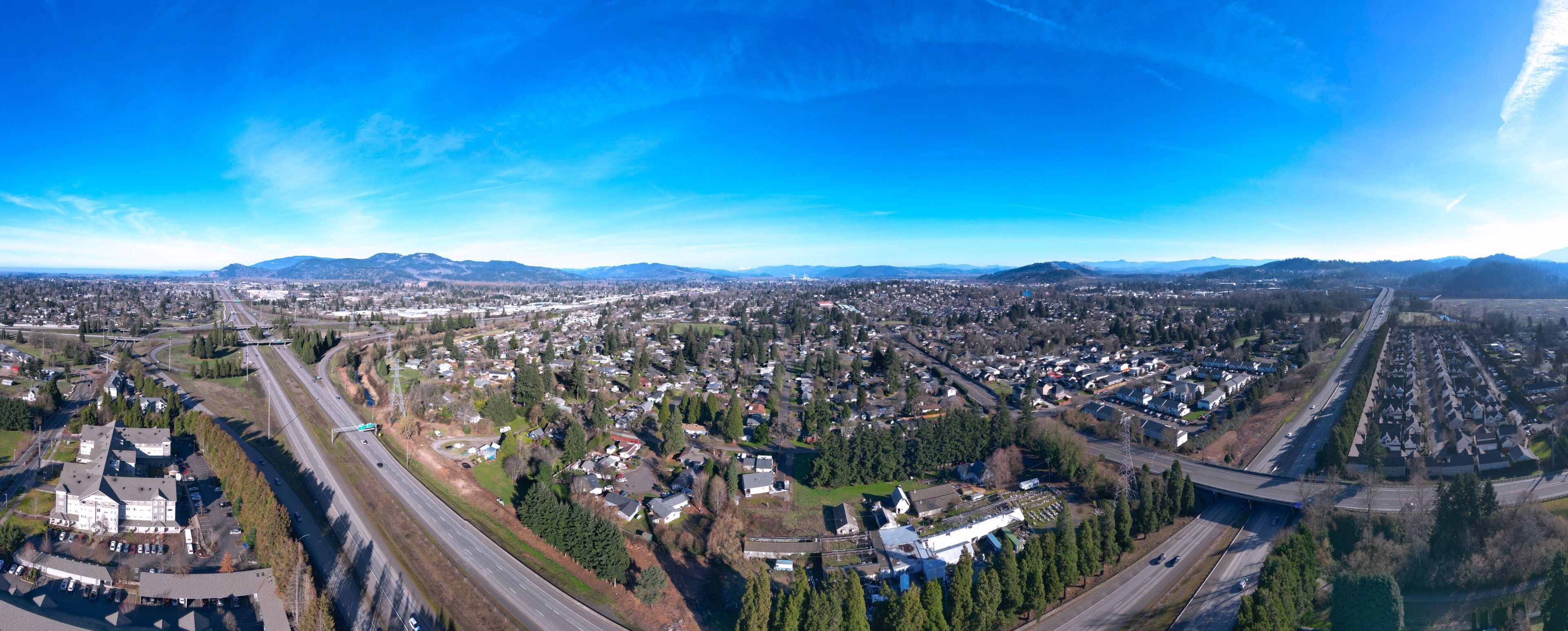 A panoramic view of a city with a highway, residential areas, and distant mountains.