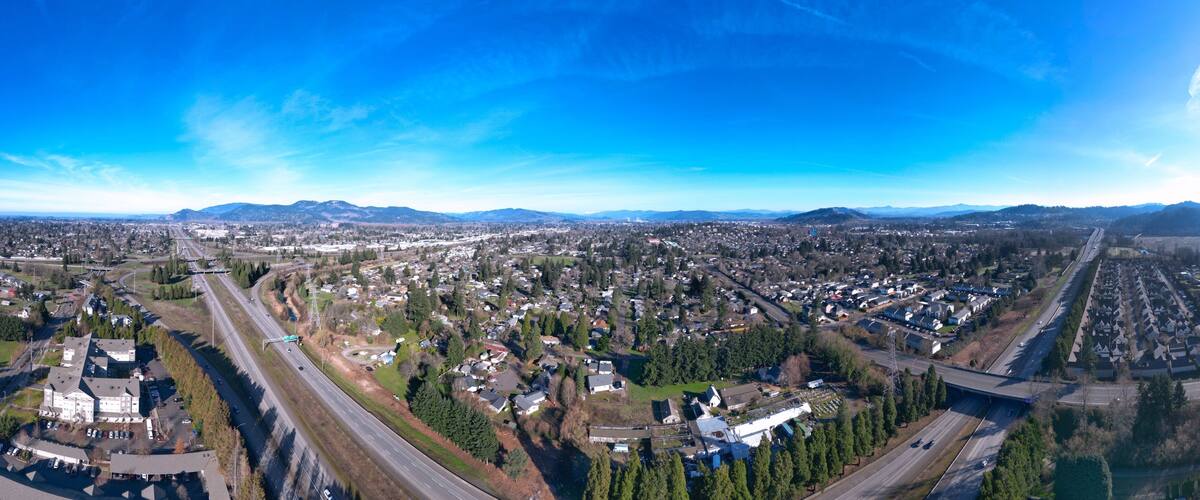 A panoramic view of a city with a highway, residential areas, and distant mountains.