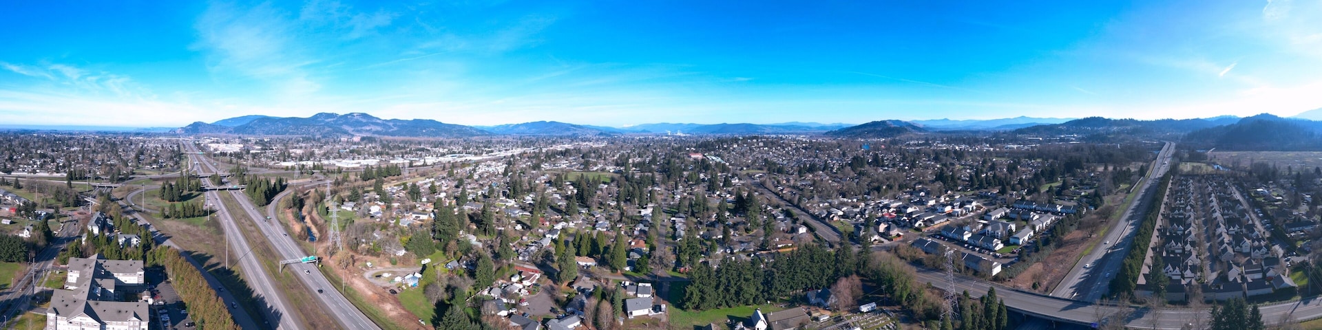A panoramic view of a city with a highway, residential areas, and distant mountains.