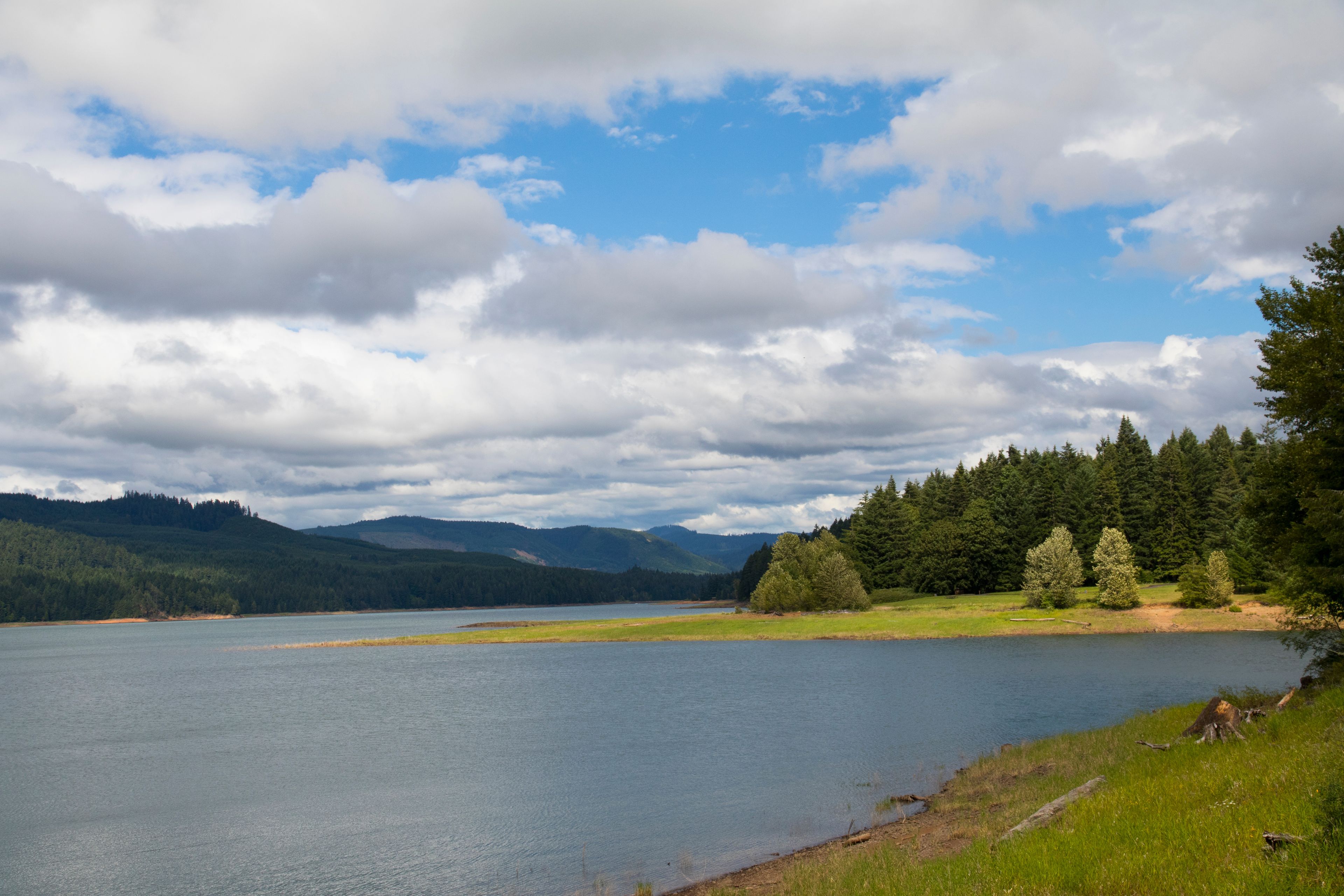 Ein See, umgeben von bewaldeten Hügeln und einem teilweise bewölkten Himmel.