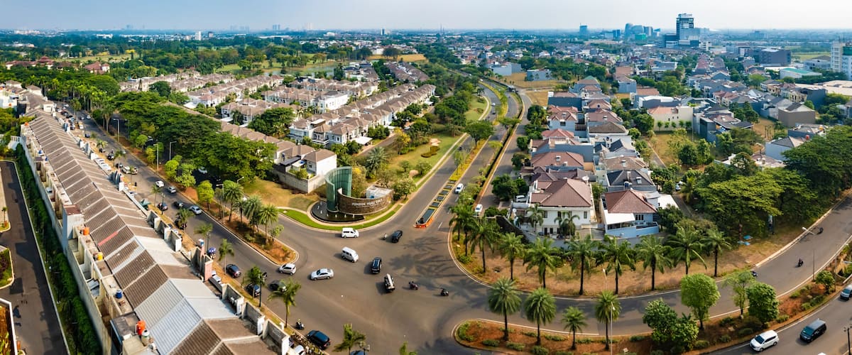 A residential area with a curved road, palm trees, and a distant city skyline.