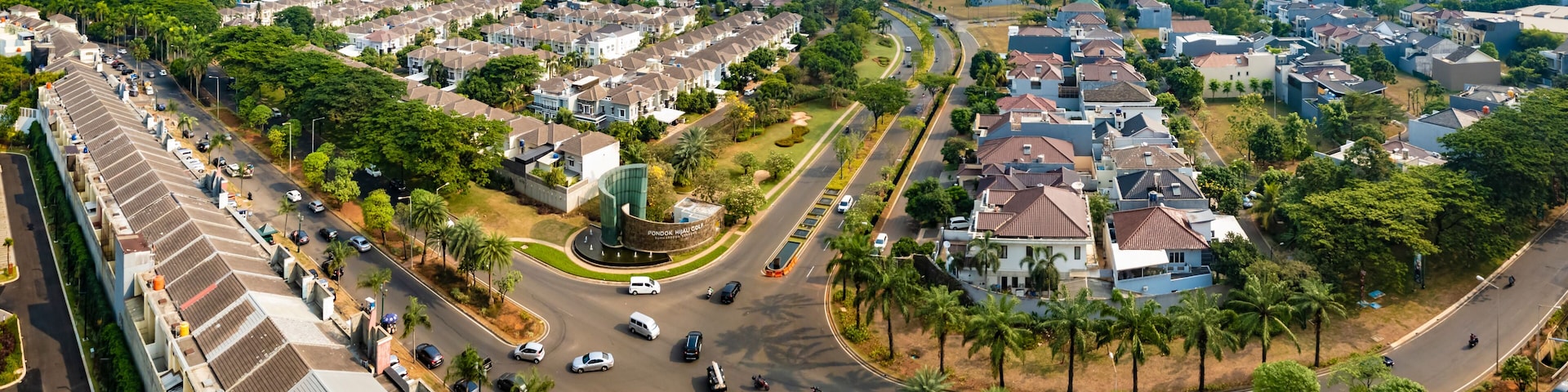 A residential area with a curved road, palm trees, and a distant city skyline.