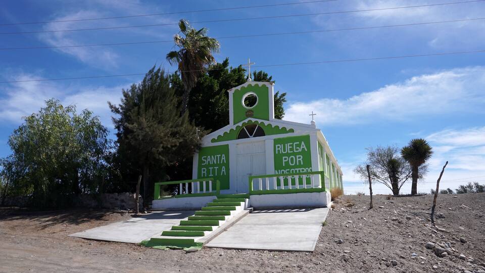 A small church with a cross on top, surrounded by trees and a clear sky.