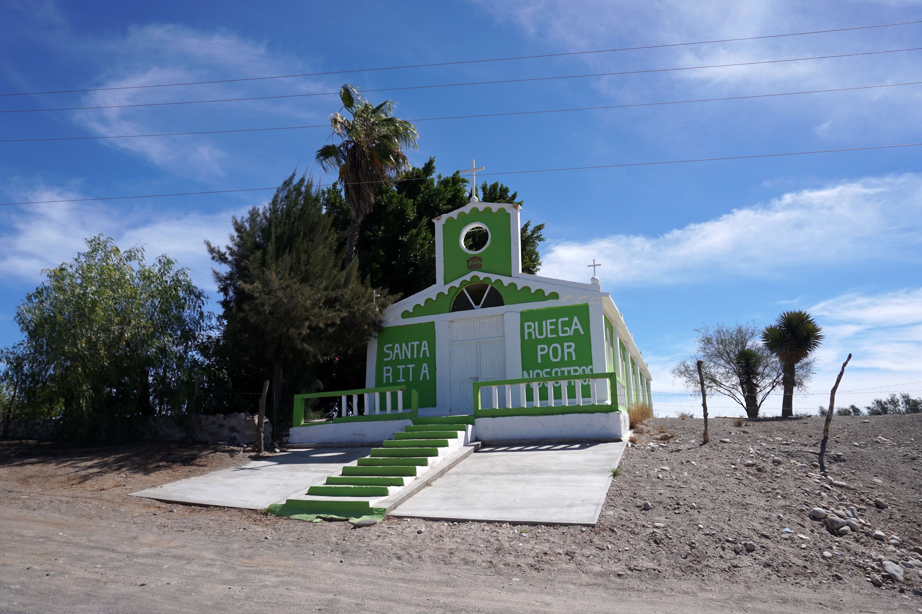 A small church with a cross on top, surrounded by trees and a clear sky.