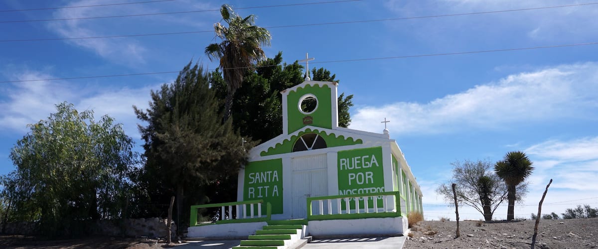 A small church with a cross on top, surrounded by trees and a clear sky.
