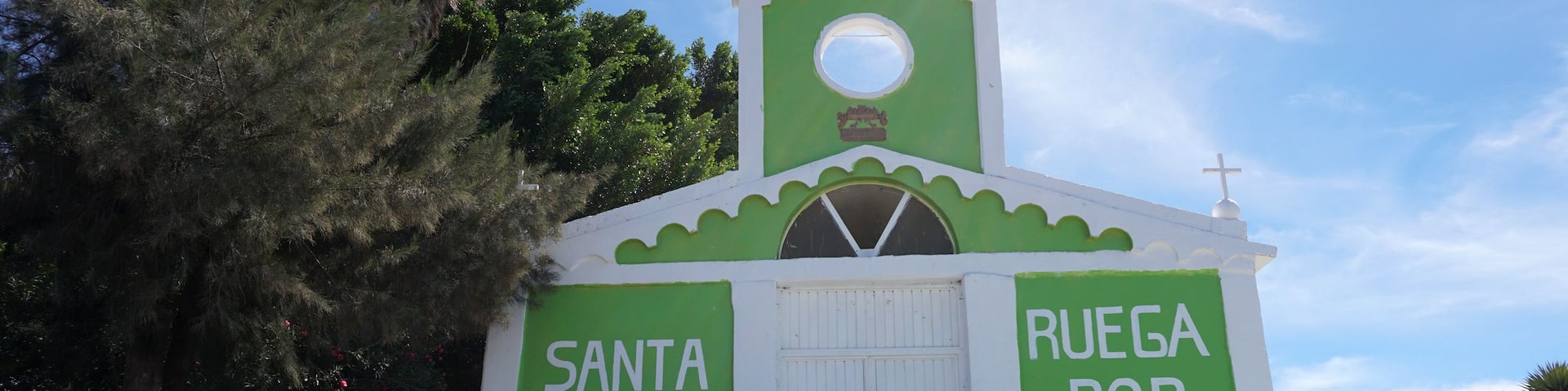 A small church with a green and white facade, a cross on top, and the words 'Santa Rita' and 'RUEGA POR NOSTROS' on the sides.