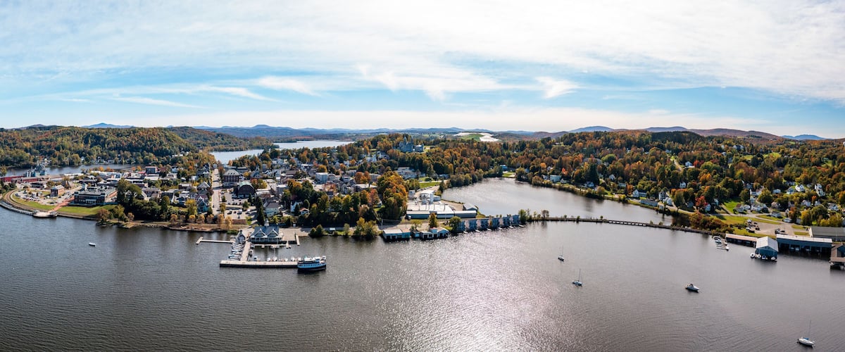 A lakeside town with a dock, boats, and autumn-colored trees.