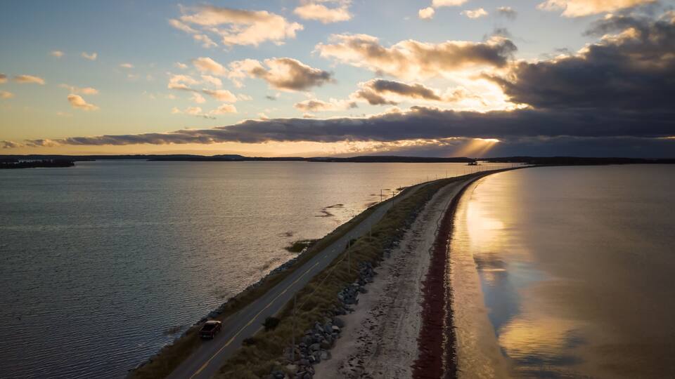 A coastal road with a bridge over water, surrounded by a calm sea and a cloudy sky.