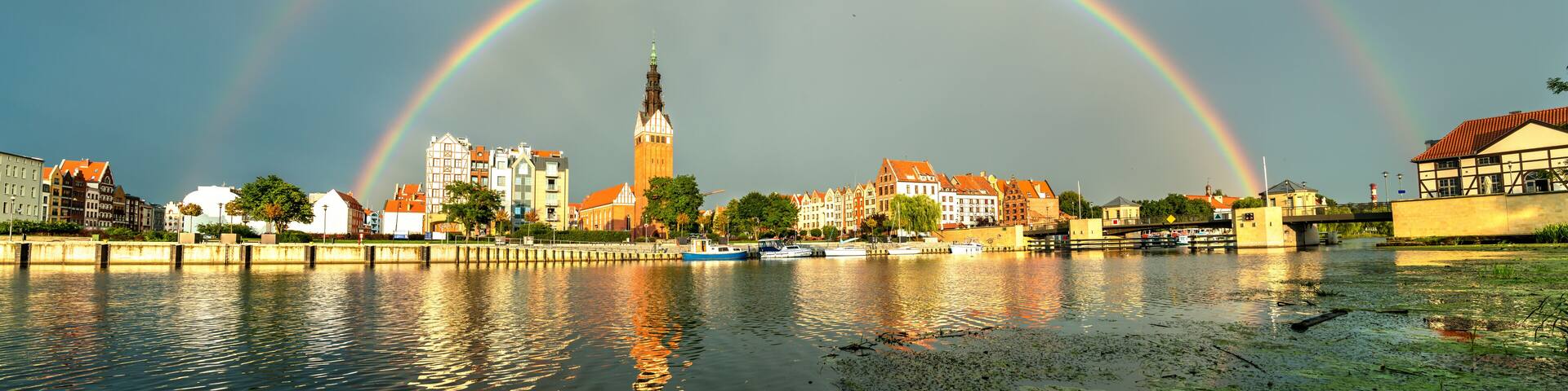 A cityscape with a prominent tower and a rainbow arching over a river.