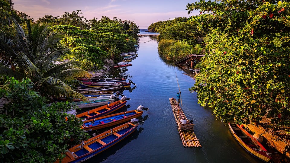 A river with boats docked along the banks, surrounded by lush greenery and trees.
