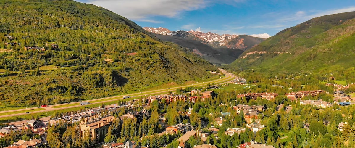 A mountainous landscape with a valley, a road, and a cluster of buildings.