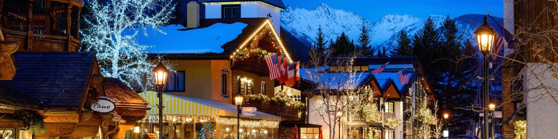 A snow-covered town square with illuminated buildings and a prominent hotel.