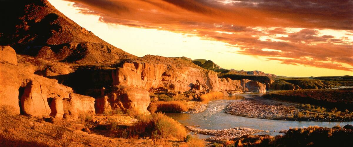 A river flowing through a canyon with rocky cliffs and a sunset sky.