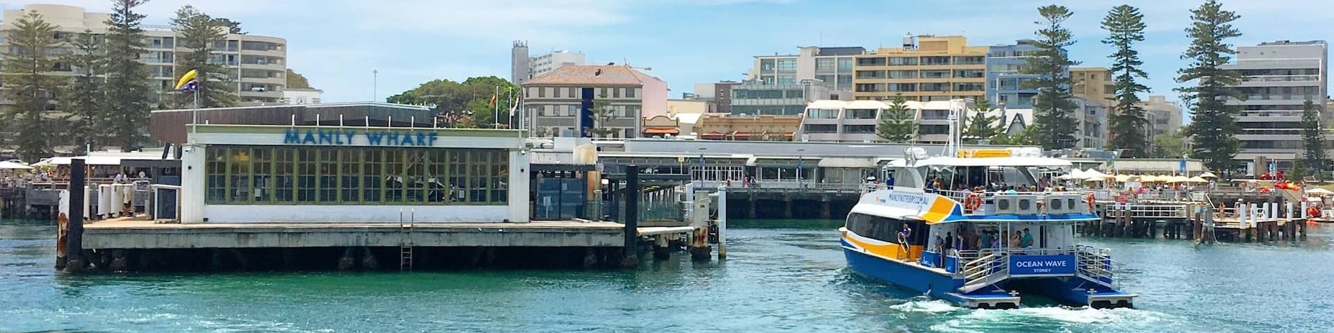 A waterfront with a ferry named 'Ocean Wave' and a building labeled 'MANYLY WHARF'.